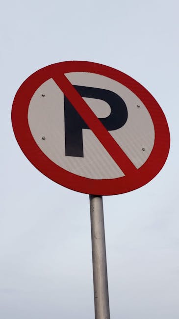 A circular no parking sign with a red border and a black letter 'P' crossed out by a red diagonal line, mounted on a metal pole against a cloudy grey sky. This sign indicates parking restrictions in the area, which could impact house removals and furniture transport logistics during a home relocation. Temporary parking limitations like this are relevant for professional removals services, such as those provided by Man and Van Abbey Wood, especially when planning moving activities on narrow streets or areas with specific parking rules. Proper planning for loading and unloading areas is essential to ensure smooth packing and moving processes, including loading furniture, boxes, and appliances into vans or trucks. The image highlights the importance of adhering to parking regulations to facilitate efficient house removals, particularly in urban or congested settings like Abbey Wood, especially when coordinating with removal professionals for a detailed SE2 flat removals guide.